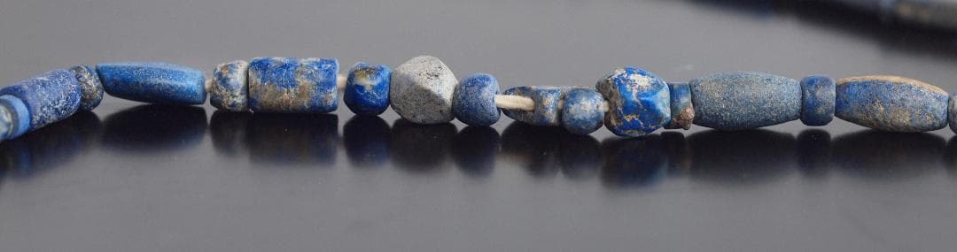古代濃紺ラピスの管玉や丸玉をほぼ左右対称に編み、トップに斧型や多面体、80個の連